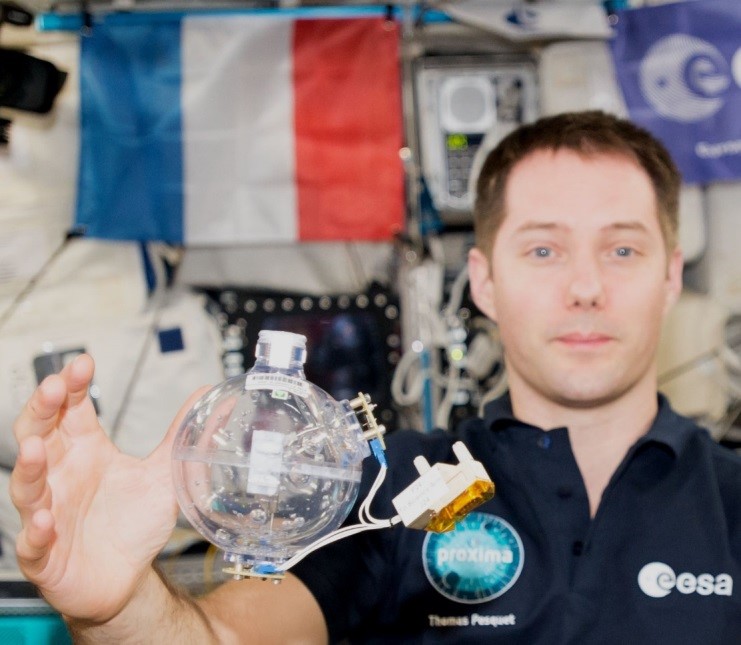 Thomas Pesquet présente le réservoir utilisé dans l’expérience Fluidics. La sphère est partiellement remplie d’eau pour étudier la turbulence d’ondes capillaires. © ESA/CNES